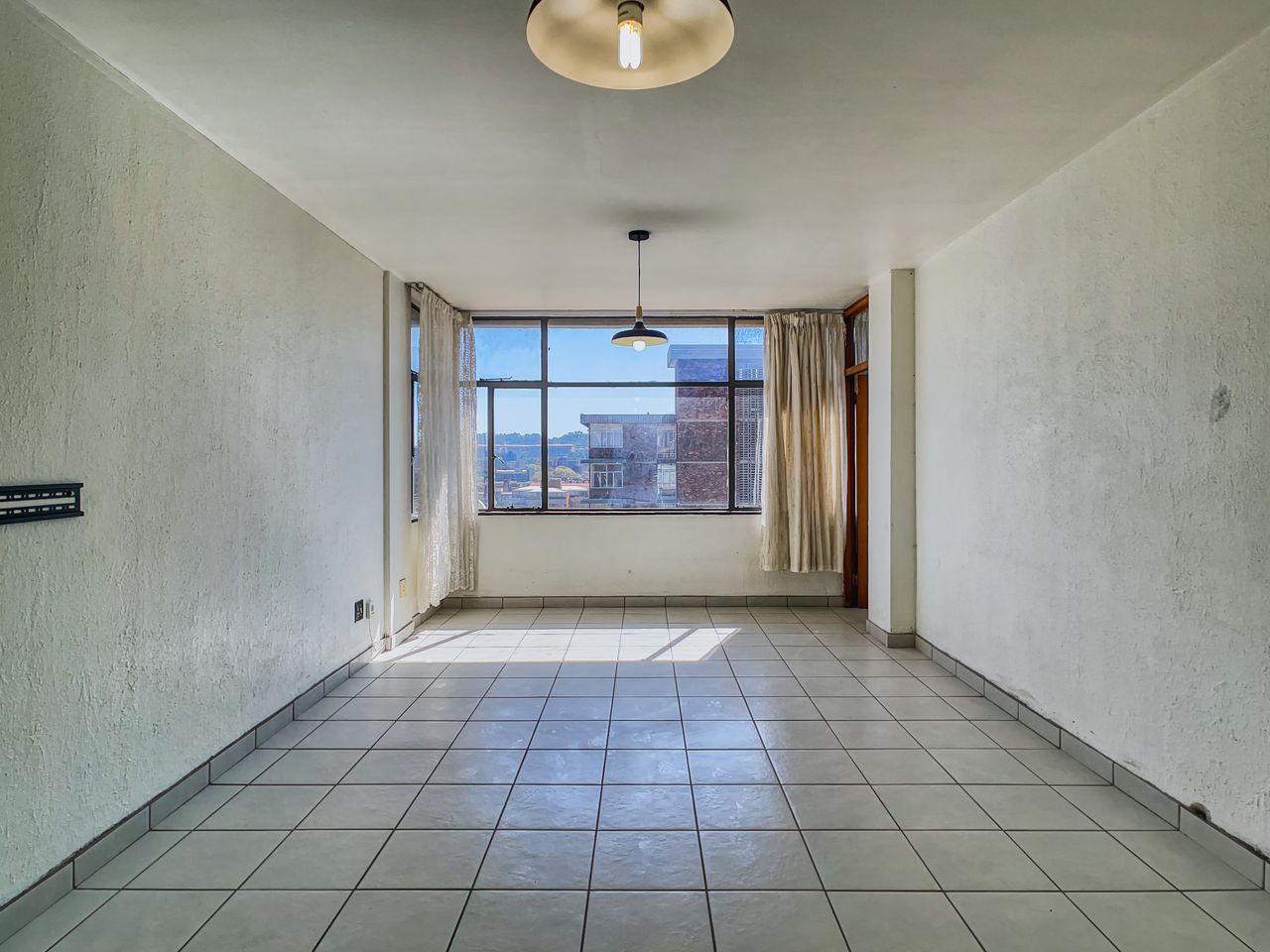 Bright empty room featuring tiled flooring, a large window, and pendant lighting, perfect for real estate listings.